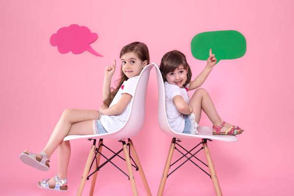 two little girls against a coloured wall with speech bubbles above their heads