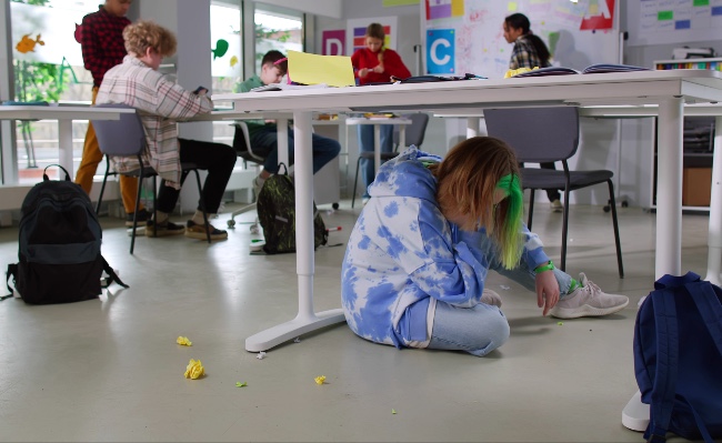 Stressed teen hides under table in classroom - disruptive classroom behaviour